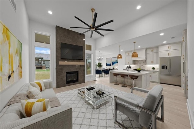 living room with a large fireplace, sink, ceiling fan with notable chandelier, and light wood-type flooring