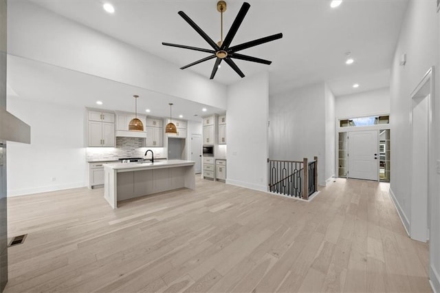 kitchen with tasteful backsplash, white cabinets, hanging light fixtures, a kitchen island with sink, and light hardwood / wood-style flooring