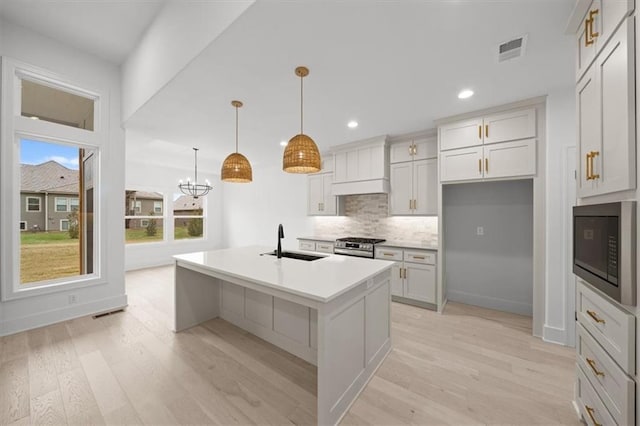 kitchen with built in microwave, sink, custom exhaust hood, decorative light fixtures, and a center island with sink