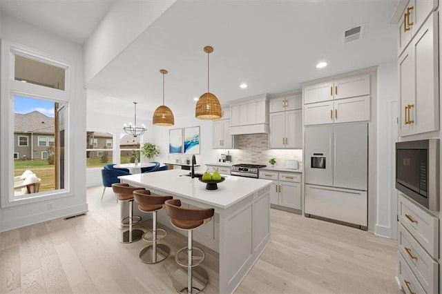 kitchen featuring pendant lighting, a breakfast bar area, premium range hood, built in appliances, and a center island with sink