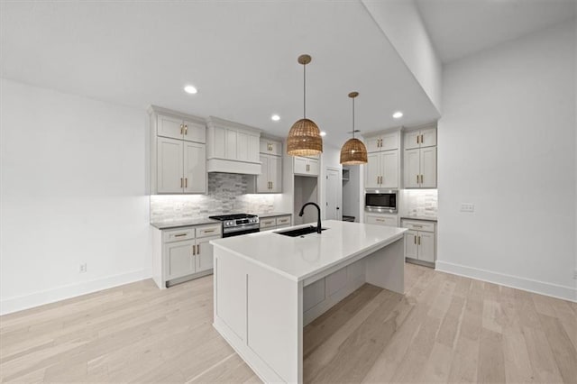 kitchen with decorative light fixtures, an island with sink, sink, decorative backsplash, and stainless steel appliances