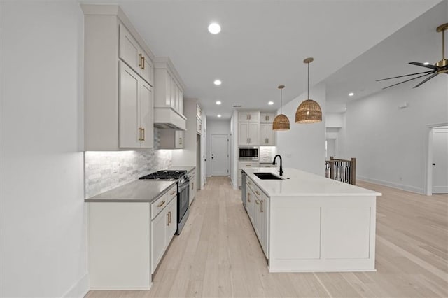 kitchen featuring decorative light fixtures, white cabinetry, sink, stainless steel appliances, and a center island with sink