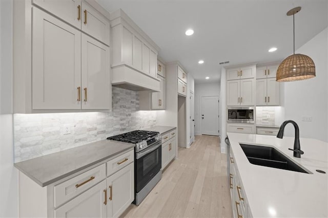 kitchen featuring pendant lighting, stainless steel gas stove, built in microwave, white cabinetry, and sink