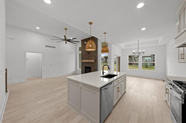 kitchen with pendant lighting, sink, a large fireplace, stainless steel appliances, and a center island with sink