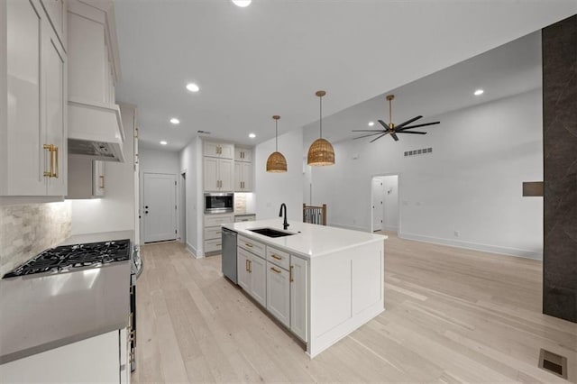 kitchen with white cabinetry, stainless steel appliances, decorative light fixtures, and a kitchen island with sink