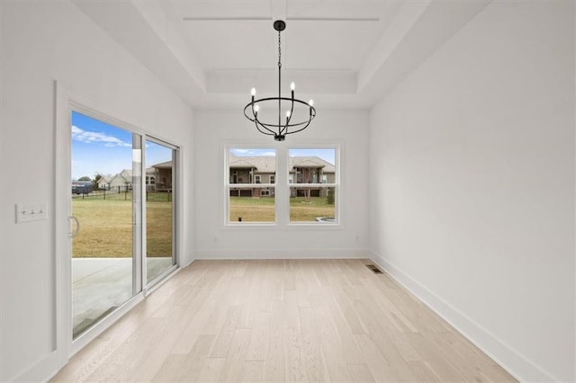 unfurnished dining area with a notable chandelier, a tray ceiling, and light wood-type flooring