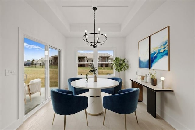 dining area with a raised ceiling, an inviting chandelier, and light hardwood / wood-style floors