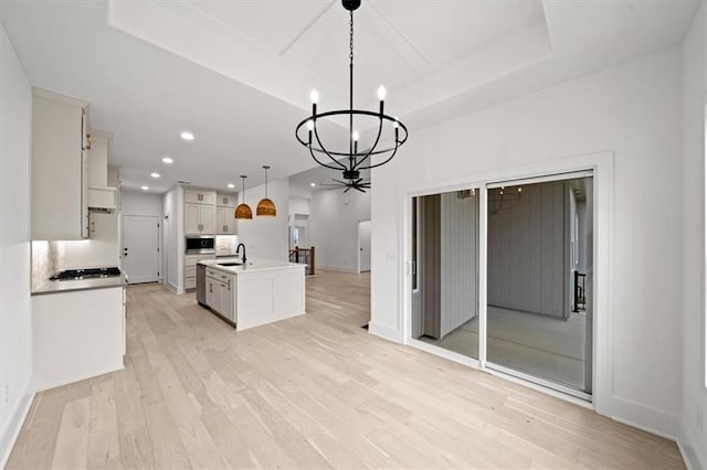 kitchen with sink, a raised ceiling, pendant lighting, a kitchen island with sink, and white cabinets