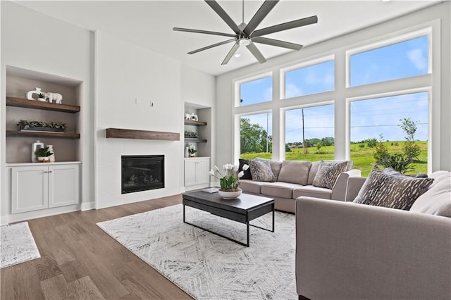 living room with a fireplace, wood-type flooring, built in features, and ceiling fan