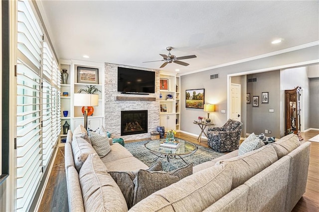 living room featuring ceiling fan, a stone fireplace, built in features, hardwood / wood-style floors, and ornamental molding