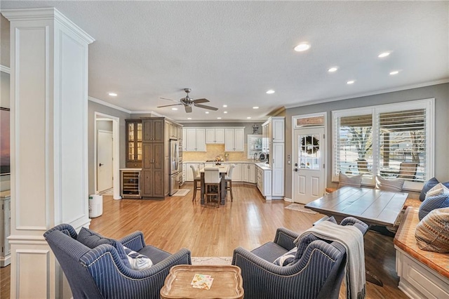 living room with ceiling fan, ornamental molding, wine cooler, and light hardwood / wood-style flooring