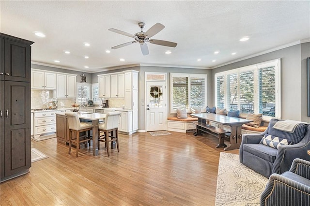 living room with crown molding, light hardwood / wood-style flooring, ceiling fan, and sink