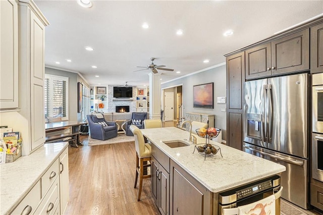 kitchen featuring appliances with stainless steel finishes, ornamental molding, ceiling fan, sink, and a stone fireplace