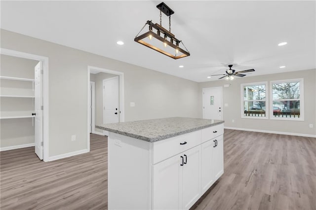 kitchen with a kitchen island, white cabinetry, hanging light fixtures, ceiling fan, and light hardwood / wood-style flooring