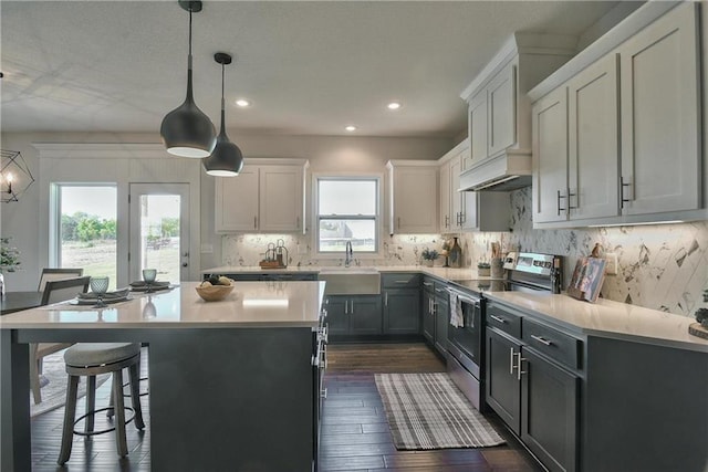 kitchen featuring backsplash, electric stove, sink, decorative light fixtures, and a kitchen island