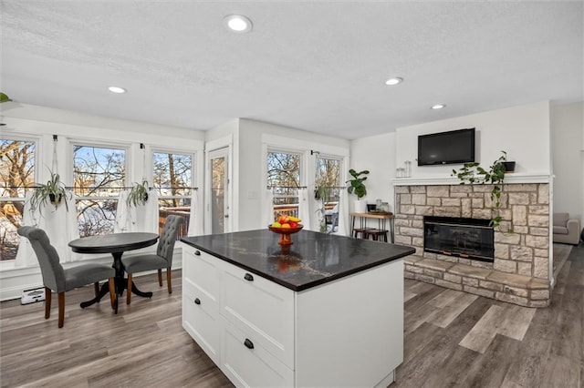 kitchen with dark countertops, wood finished floors, a fireplace, white cabinetry, and recessed lighting