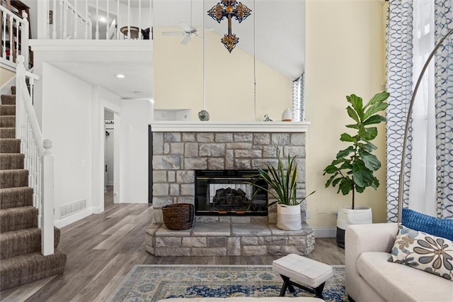 living area featuring visible vents, a high ceiling, a stone fireplace, wood finished floors, and stairs