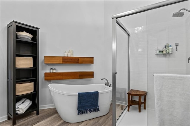 full bathroom with a stall shower, a soaking tub, baseboards, and wood finished floors