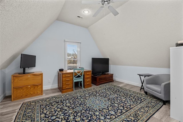 office space featuring visible vents, vaulted ceiling, light wood-style flooring, and a textured ceiling