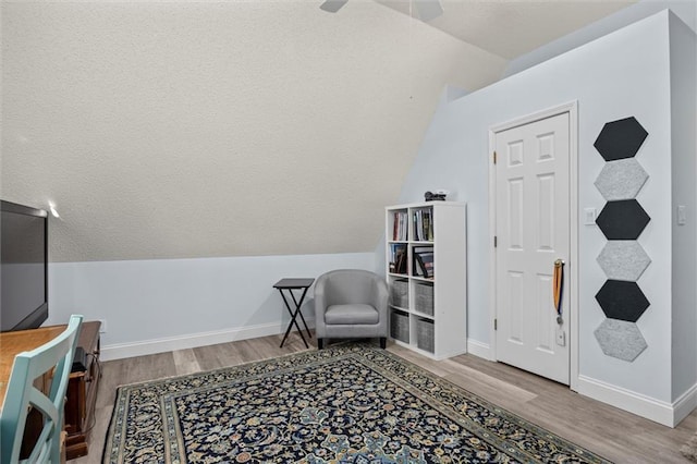 living area featuring lofted ceiling, baseboards, and wood finished floors