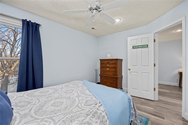 bedroom featuring visible vents, ceiling fan, a textured ceiling, wood finished floors, and baseboards