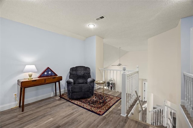 living area with visible vents, vaulted ceiling, wood finished floors, and an upstairs landing