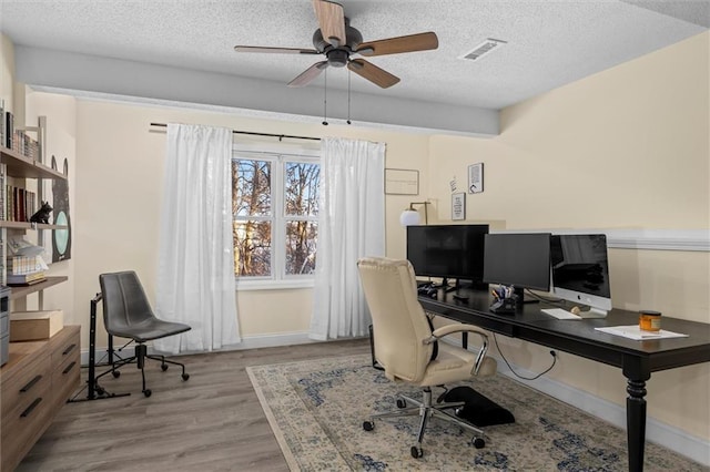 office space with a textured ceiling, ceiling fan, wood finished floors, visible vents, and baseboards