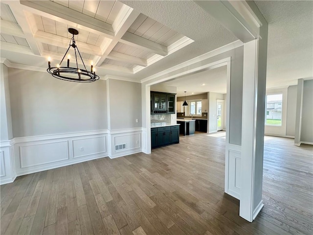 unfurnished dining area with sink, coffered ceiling, beamed ceiling, a notable chandelier, and hardwood / wood-style floors