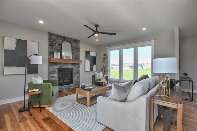 living room with a stone fireplace, ceiling fan, a textured ceiling, and hardwood / wood-style flooring