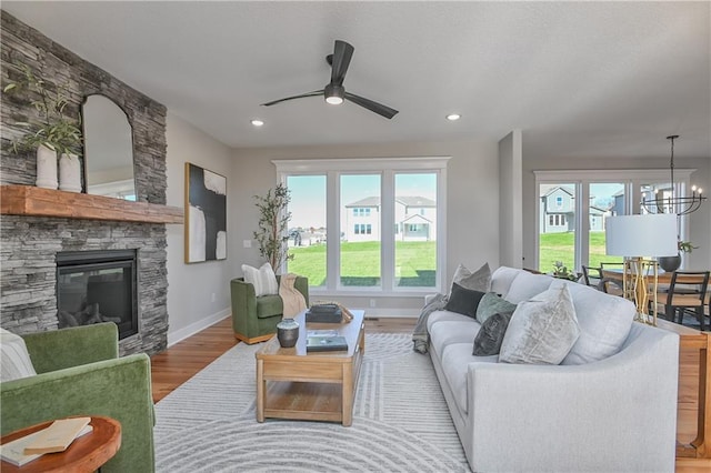 living room featuring ceiling fan with notable chandelier, a stone fireplace, and light hardwood / wood-style flooring