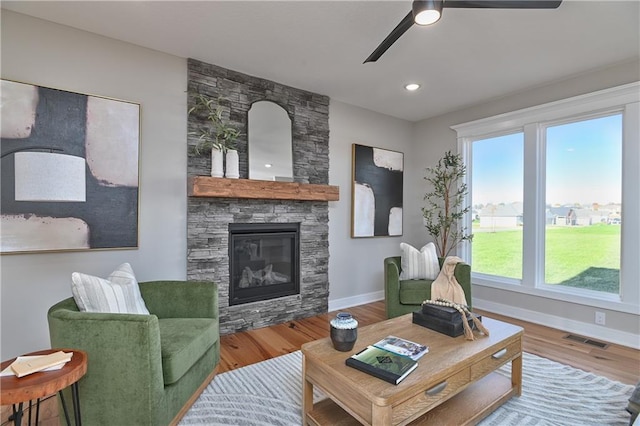 living room with a stone fireplace, a wealth of natural light, ceiling fan, and hardwood / wood-style flooring