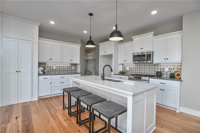 kitchen with appliances with stainless steel finishes, a kitchen island with sink, sink, decorative light fixtures, and white cabinets