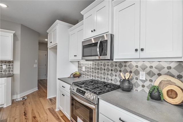 kitchen with white cabinets, light hardwood / wood-style floors, stainless steel appliances, and tasteful backsplash