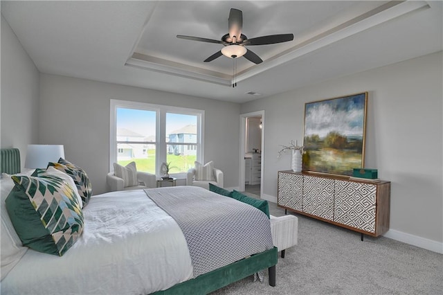 carpeted bedroom featuring a tray ceiling, ensuite bath, and ceiling fan