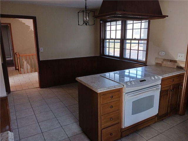 kitchen with custom exhaust hood, white range with electric stovetop, pendant lighting, light tile patterned floors, and a notable chandelier