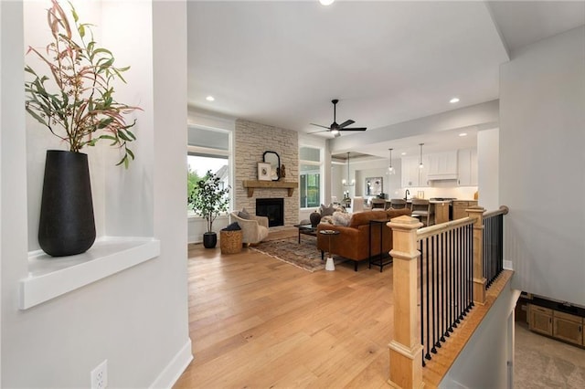 living room featuring ceiling fan, a stone fireplace, and light hardwood / wood-style floors