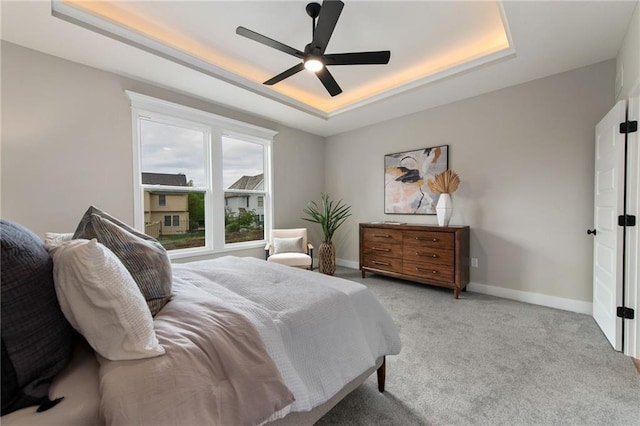 bedroom with a raised ceiling, light colored carpet, and ceiling fan