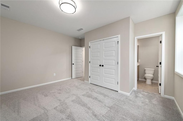 unfurnished bedroom featuring light colored carpet, ensuite bath, and a closet