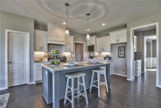 kitchen featuring dark wood-type flooring, a center island with sink, hanging light fixtures, white cabinetry, and stainless steel appliances