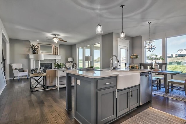 kitchen featuring pendant lighting, a kitchen island with sink, sink, stainless steel dishwasher, and gray cabinets