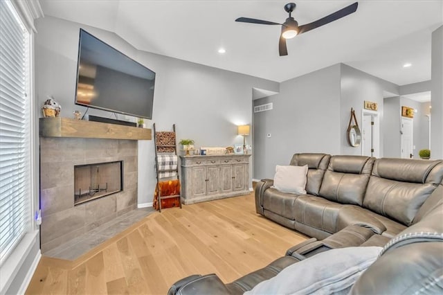 living room featuring ceiling fan, a healthy amount of sunlight, light wood-type flooring, and a tile fireplace