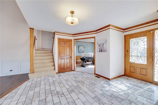 entryway featuring a wainscoted wall, visible vents, stairway, ornamental molding, and a textured ceiling