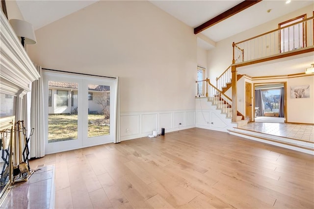 unfurnished living room with high vaulted ceiling, beamed ceiling, stairway, and wood finished floors