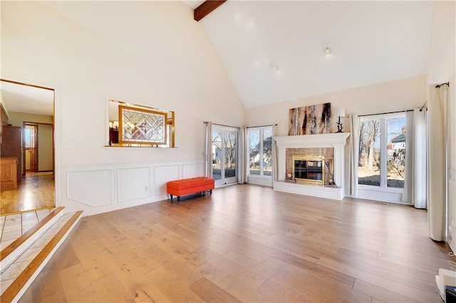 unfurnished room with wood finished floors, plenty of natural light, a glass covered fireplace, and beam ceiling