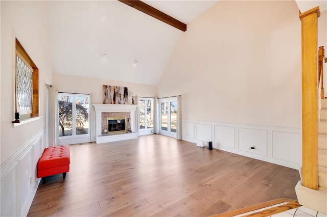 unfurnished living room featuring wood finished floors, a glass covered fireplace, beam ceiling, and a healthy amount of sunlight