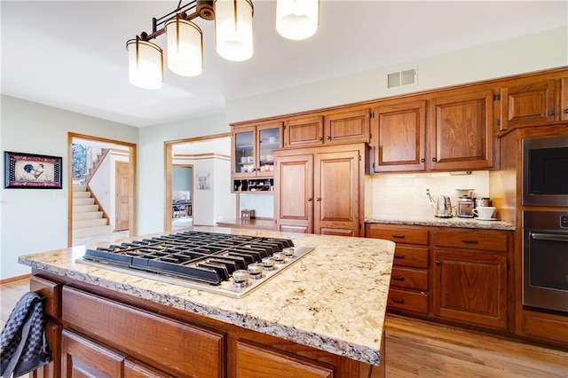 kitchen featuring tasteful backsplash, visible vents, brown cabinetry, light wood-type flooring, and stainless steel gas stovetop