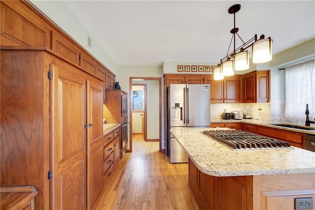 kitchen with appliances with stainless steel finishes, light wood-style floors, brown cabinets, and a sink