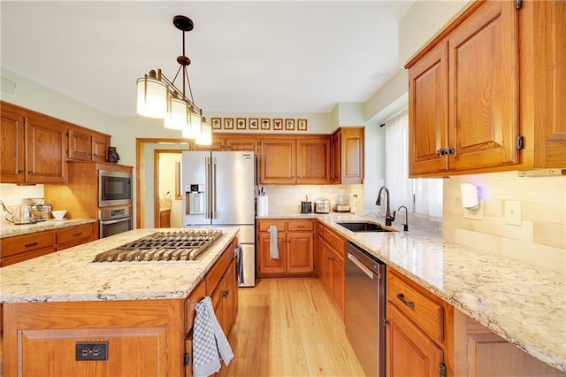 kitchen featuring appliances with stainless steel finishes, brown cabinets, a sink, and light stone counters