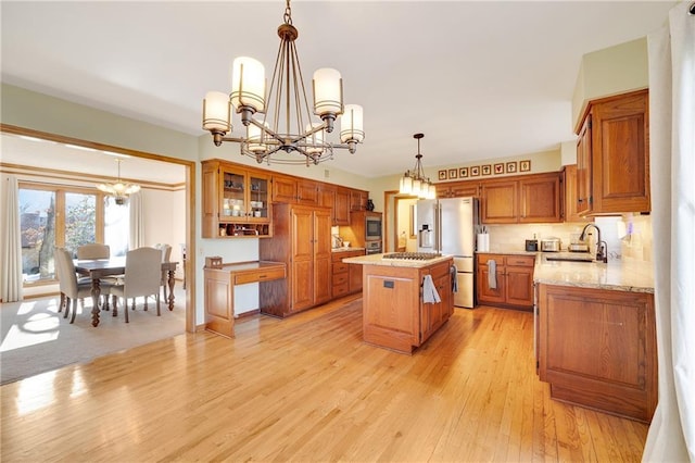 kitchen featuring a kitchen island, brown cabinets, an inviting chandelier, stainless steel appliances, and light wood-style floors