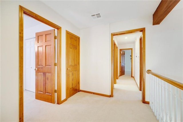 hallway featuring visible vents, baseboards, and light colored carpet